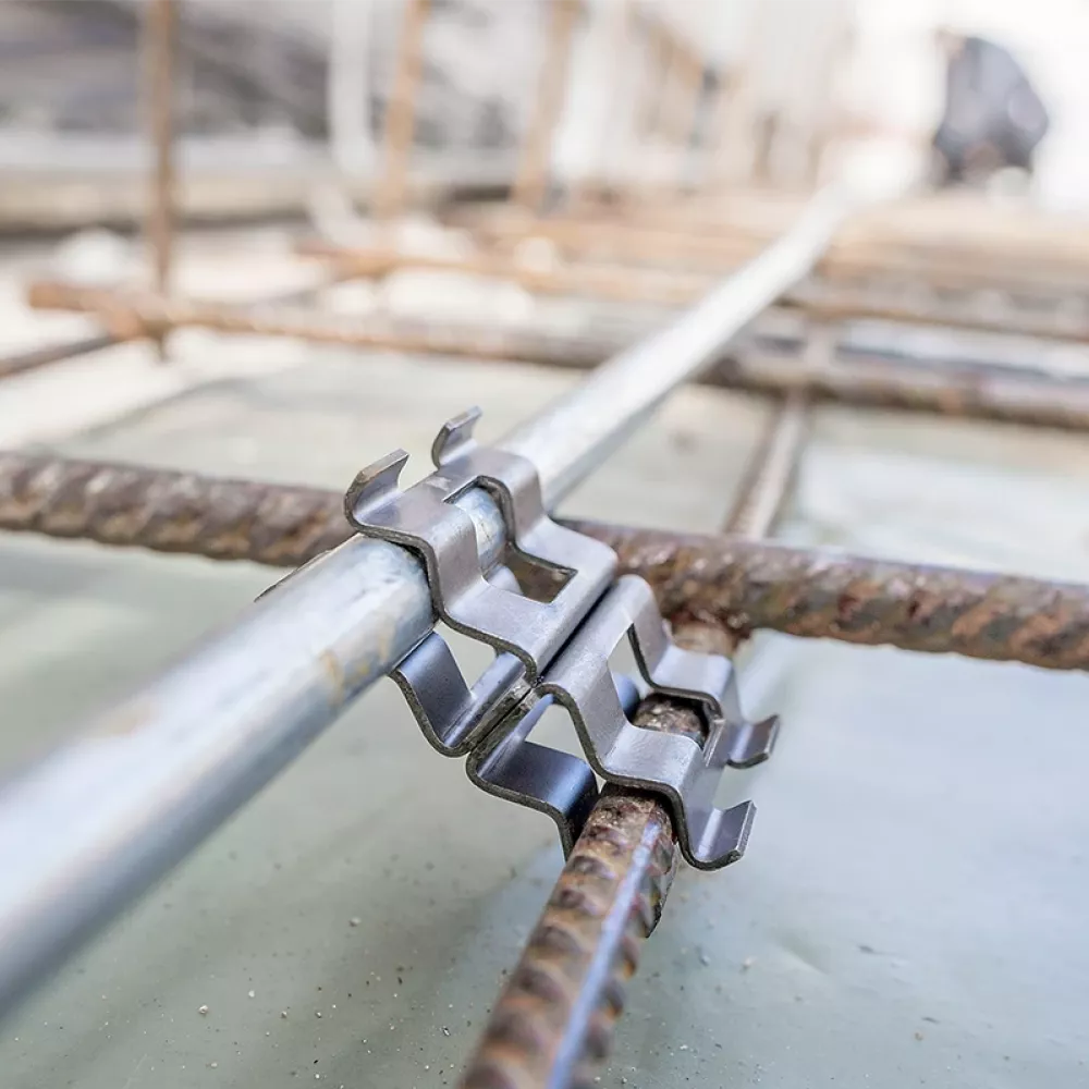 Close-up of a metal grounding clamp connecting a steel conductor to reinforcing rebar embedded in a concrete foundation slab.